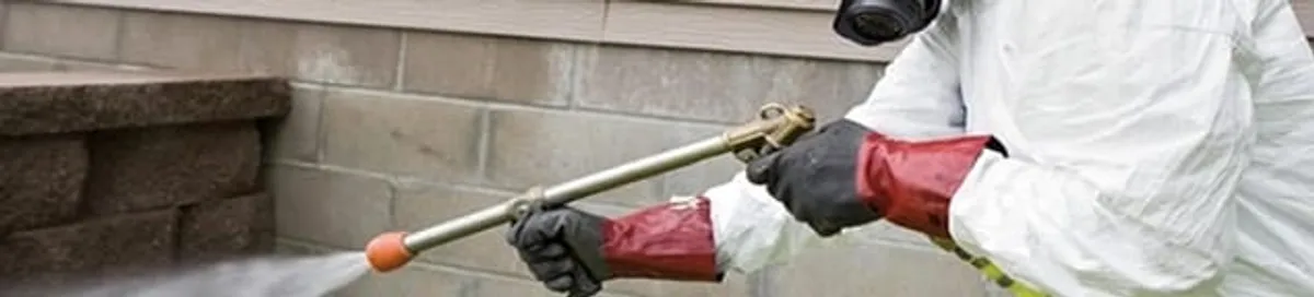 Pest control technician applying exterior insect treatment along a home foundation in Salt Lake City, UT
