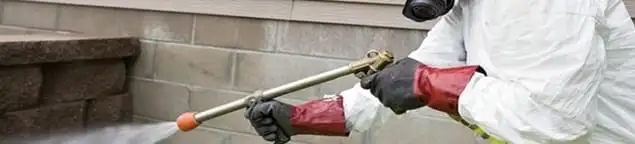 Pest control technician applying exterior insect treatment along a home foundation in Salt Lake City, UT