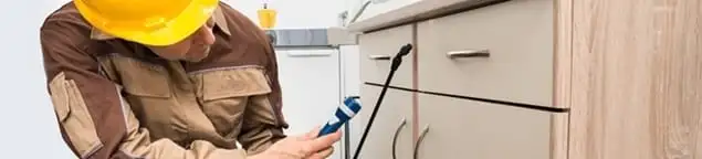 Roach exterminator applying treatment under kitchen cabinets in Salt Lake City, UT