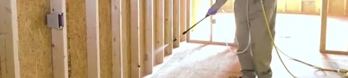 Termite treatment technician applying spray along framing and unfinished walls in Salt Lake City, UT