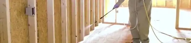 Termite treatment technician applying spray along framing and unfinished walls in Salt Lake City, UT